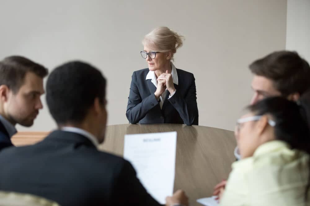Stressed older woman in the middle of a job interview while young executives review her resume