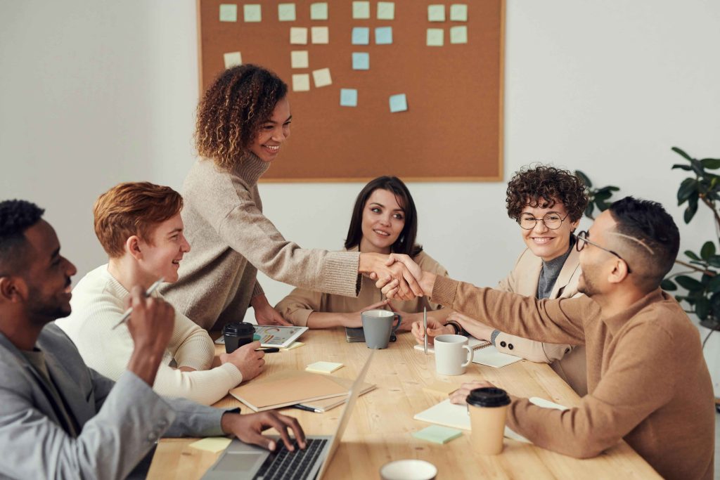 workers at a table in a meeting smiling and shaking hands